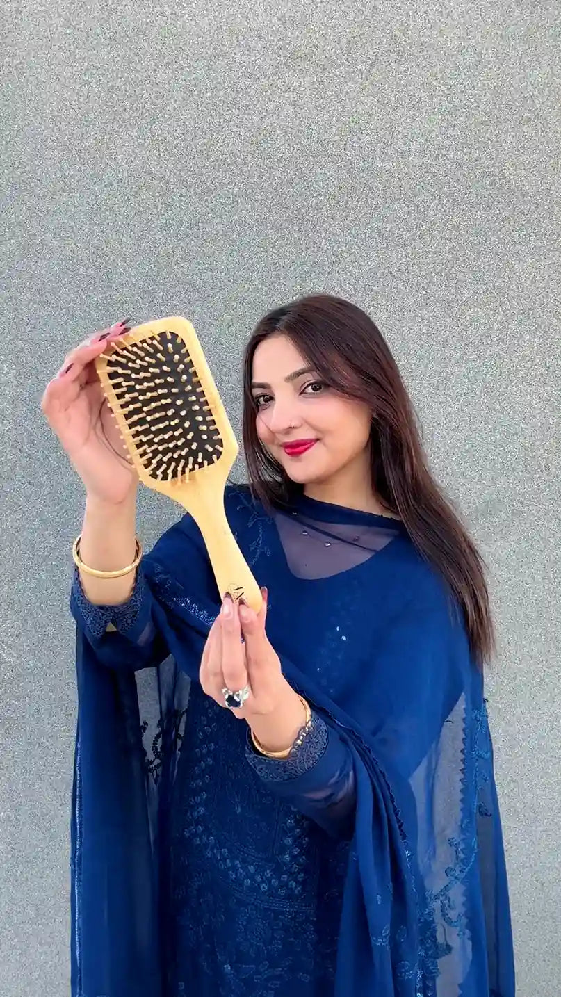 Just Amna large wooden hairbrush held by model in blue embroidered outfit, gray backdrop