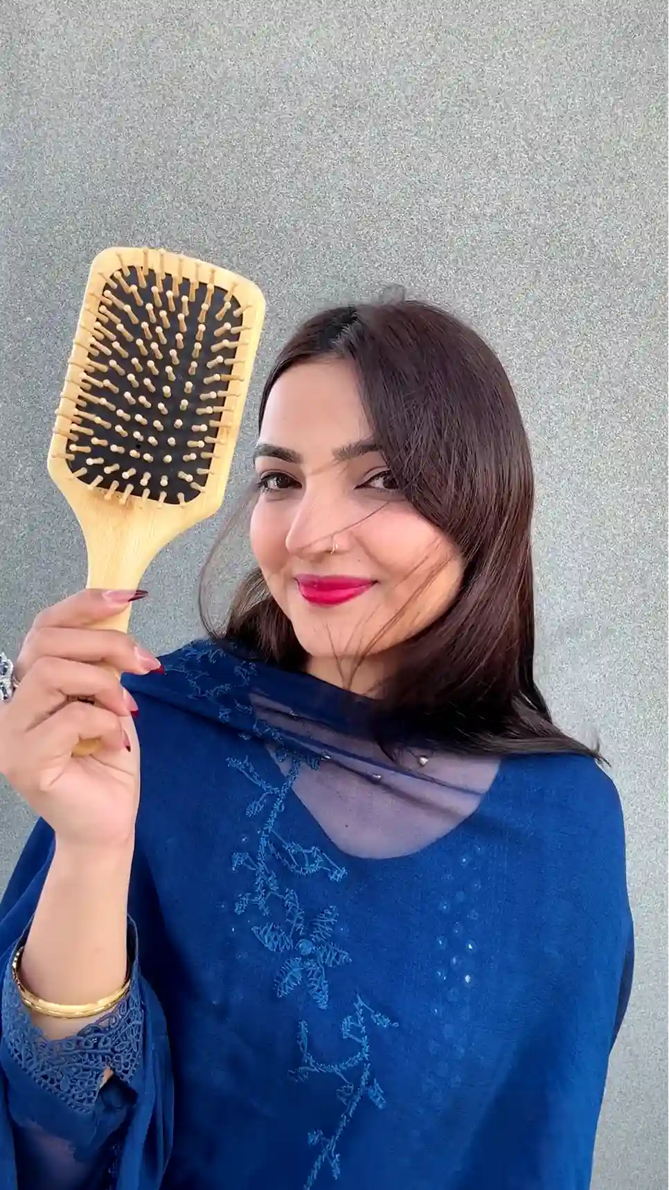 Just Amna wooden paddle hairbrush held by model, beige bristles and black cushion