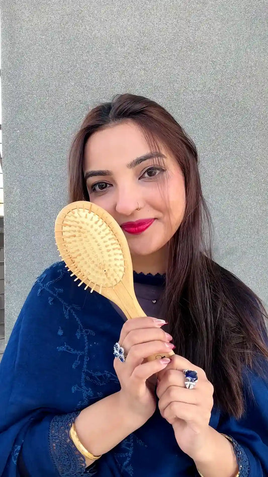 Woman holding a Just Amna bamboo hair brush for smooth, healthy hair.