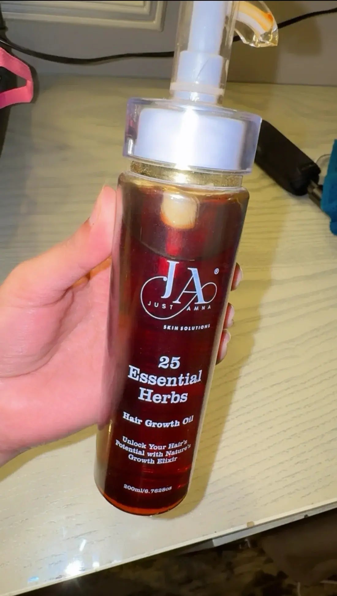 Hand holding Just Amna skin solutions hair growth oil for daily use.