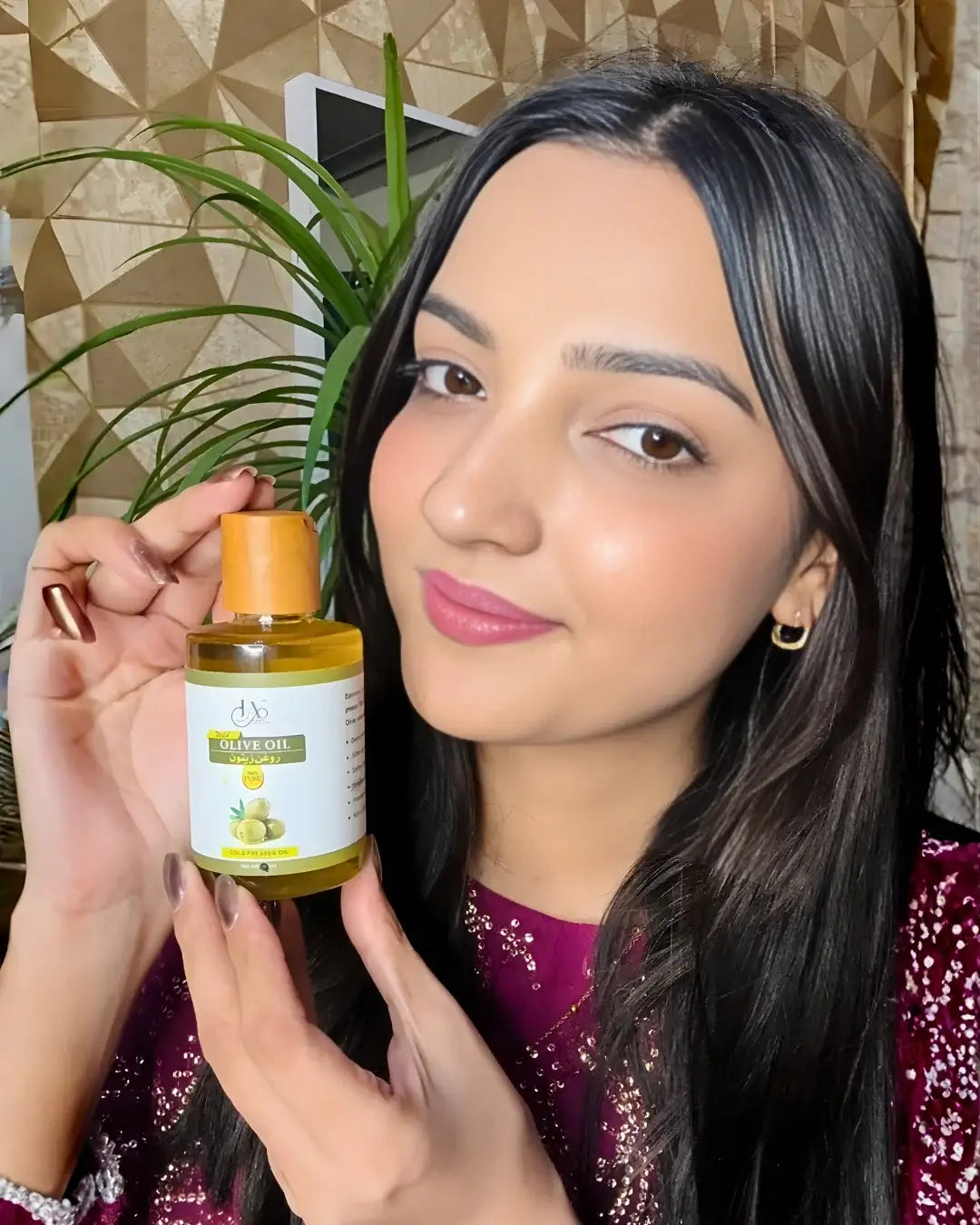 Woman showcasing a bottle of Just Amna Olive Oil for hair and skin care.