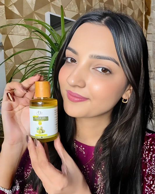 Woman showcasing a bottle of Just Amna Olive Oil for hair and skin care.