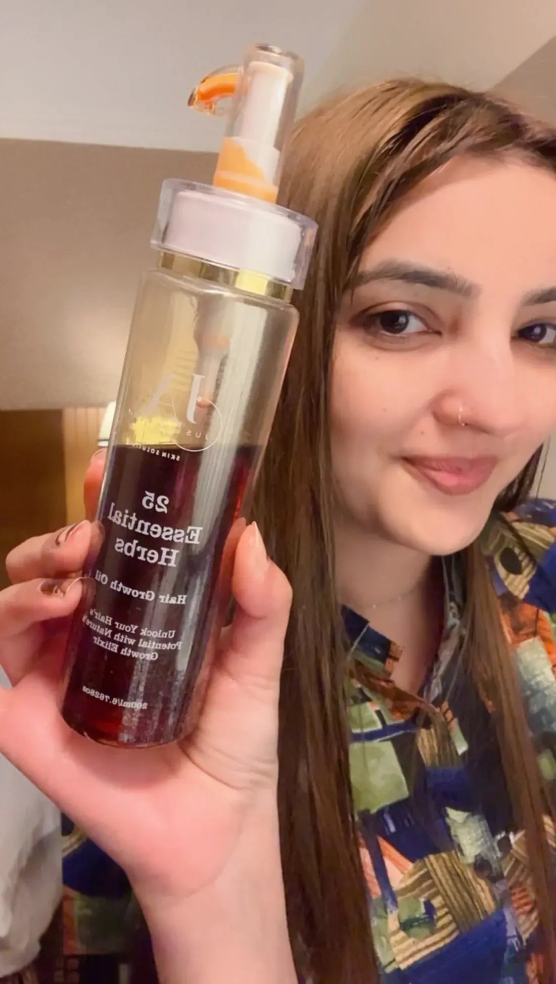 Woman holding a bottle of Just Amna hair growth elixir for scalp care.